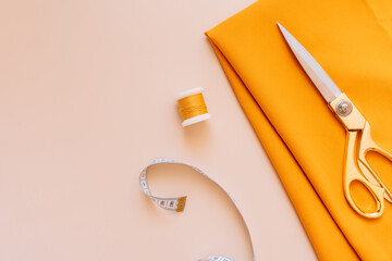 Sewing scissors lie on an orange fabric next to threads and a measuring tape.