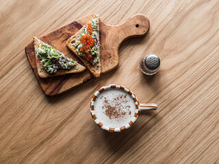 Delicious breakfast, brunch, snack - cappuccino and avocado red caviar bruschetta on a wooden table, top view
