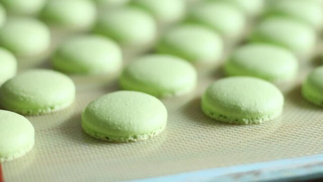 Showing pastel green freshly baked macaroons on baking tray. French homemade macarons dessert making process. 