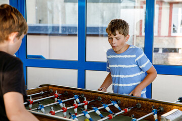 Two smiling school boys playing table soccer. Happy excited children having fun with family game...