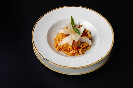 Hearty Italian pasta dish with tomato sauce and basil leaves on a white plate on a black background