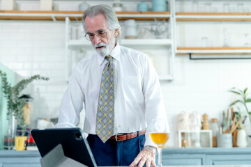 Seasoned professional with a drink pauses to view content on his tablet in a contemporary home kitchen.