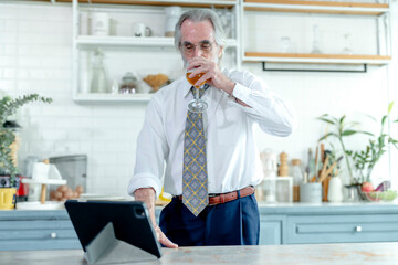 Seasoned professional with a drink pauses to view content on his tablet in a contemporary home kitchen.