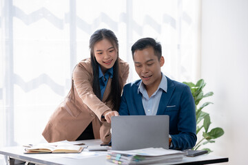 Two young asian business people using a laptop together while sitting in a meeting.