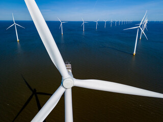 A group of windmills floats gracefully on top of tranquil waters in the Netherlands Flevoland, a picturesque scene captured in Spring. drone aerial vie w of windmill turbines green energy in the ocean
