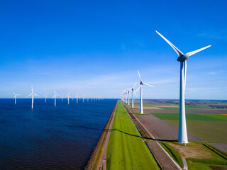 A serene scene of a row of wind turbines standing tall next to a calm body of water in Flevoland, the Netherlands, during the vibrant season of Spring. green energy in the ocean