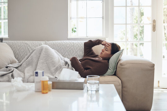Woman, sick and headache with medication on sofa for flu, cold or sinus in living room at home. Tired female person with illness, fever or influenza in fatigue or asleep on couch from paracetamol