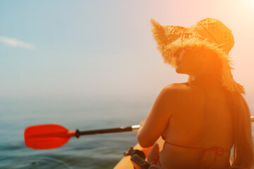 A woman wearing a straw hat is paddling a canoe on a sunny day. Scene is relaxed and carefree, as...