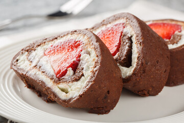 Pieces of chocolate cake roll with strawberries and cream cheese close-up on a plate. Horizontal