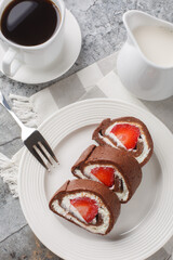 Sweet chocolate cake roll filled with strawberries and cream cheese served with coffee close-up on the table. Vertical top view from above