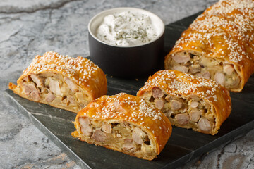 Savory strudel with chicken, mushrooms, onions and cheese served with sauce close-up on a board on...