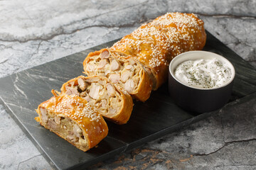 Delicious Chicken strudel with mushrooms and cheese served with sour cream sauce close-up on a board on the table. Horizontal