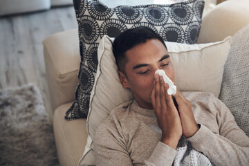 Sick, man and blowing nose with tissue for sinus, flu or illness on living room sofa above at home....