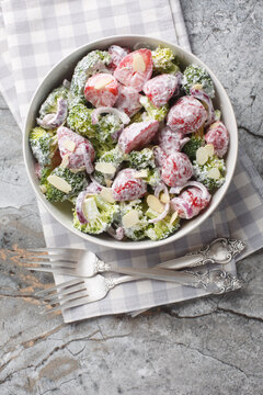 Fresh broccoli salad with strawberries, red onions and almonds dressed with yogurt close-up in a plate on the table. Vertical top view from above