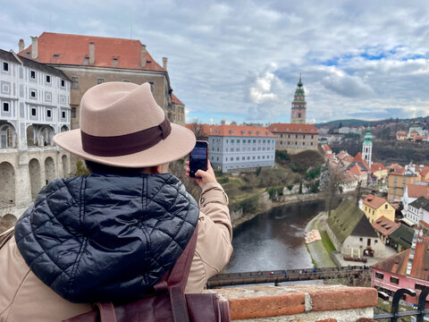 Female tourist in a hat, taking photos of Cesky Krumlov with her mobile phone