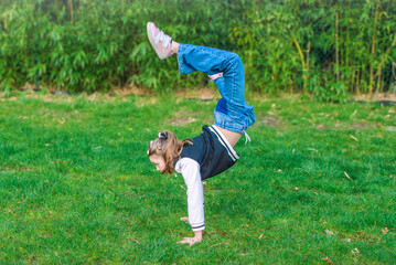 Walking gymnastics. A 10-12 year old girl tries gymnastics spontaneously during a walk in the park. - obrazy, fototapety, plakaty