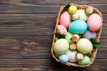 Happy Easter. Easter eggs in basket on colored table with yellow roses. Natural dyed colorful eggs background top view with copy space