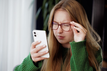 girl squinting with poor eyesight wearing glasses looking at a mobile phone at the table, concept...