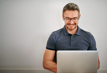 Man, freelance and wall on laptop with smile for relax in casual for social media with technology for internet. Male person, house and glasses with website for blog with mockup, writer and typing