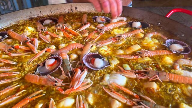 Cooking a huge traditional Spanish seafood Paella dish with shrimps, St Jacques scallops and Cigala Norway lobsters Nephrops norvegicus, delicious cooked rice with seafood, Marbella Spain, 4K shot