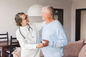 Female professional doctor showing medical test result explaining prescription using clipboard visiting senior elderly old man patient at home sitting on sofa - 781102700