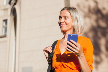 Happy middle aged woman outside in city with mobile phone