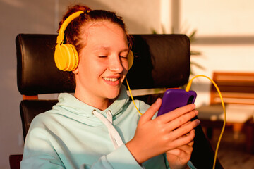 Beautiful young woman in headphones sits on sofa and enjoys listening to music