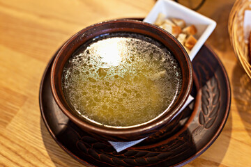 Bowl of homemade chicken broth or soup, served in traditional carved clay bowl, conveys simplicity and warmth of home-cooked meal, accompanied by side of croutons