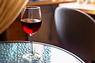 Elegant glass of red wine on textured glass table illuminated by diffused lighting. It evokes feeling of refined dinner and refined relaxation in modern setting