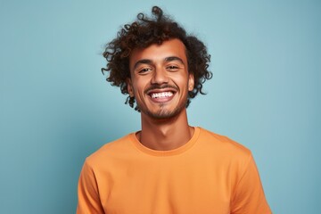 A man with curly hair and a beard is smiling and wearing an orange shirt