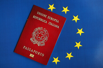 Italian passport of European Union on blue flag background close up. Tourism and citizenship concept