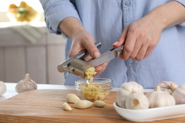 Woman squeezing garlic with press at wooden table indoors, closeup
