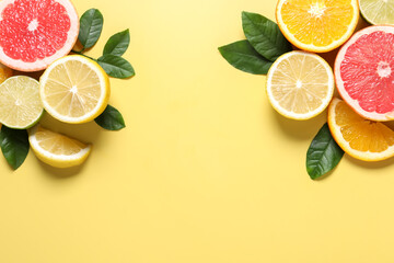Different cut citrus fruits and leaves on yellow table, flat lay. Space for text