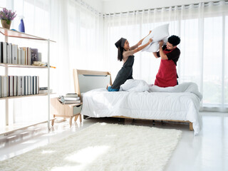 Asian playful pillow fight unfold between a smiling couple wife and husband in a modern well lit...