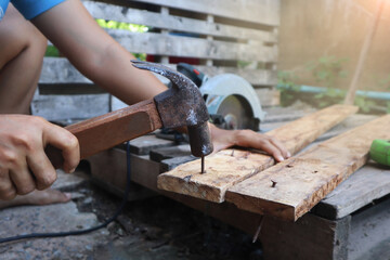 Close-up shot of nails being driven into the board. carpenter wearing a blue shirt A circular saw and a meter sharpening were placed on the side. - obrazy, fototapety, plakaty