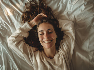 Fototapeta premium Close up of a happy young woman laying in bed with long hair on a white pillow, feeling of a morning waking, concept of good health, top view, high resolution, high quality image