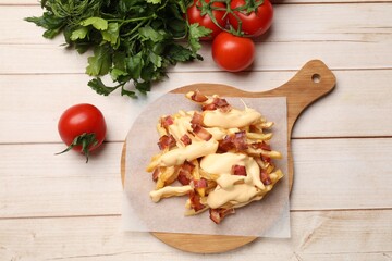Delicious French fries with bacon, cheese sauce, tomatoes and herbs on wooden table, flat lay
