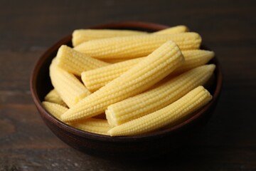 Tasty fresh yellow baby corns in bowl on wooden table