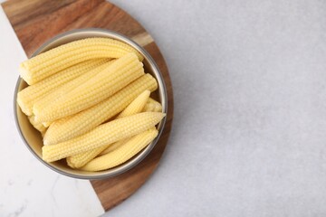 Tasty fresh yellow baby corns in bowl on white table, top view. Space for text