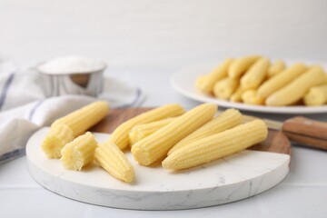 Tasty fresh yellow baby corns and knife on white tiled table, closeup