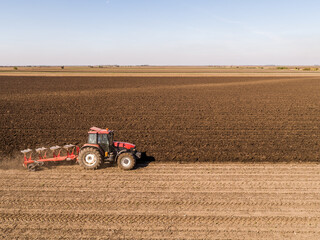 Aerial view of a tractor plowing rich soil in vast farmland during autumn season