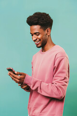 A man on a mint background in a pink sweatshirt smiles and looks at the phone
