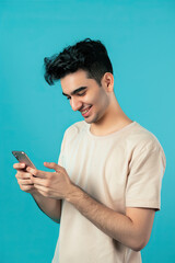 A man on a blue background in a white T-shirt smiles and looks at the phone
