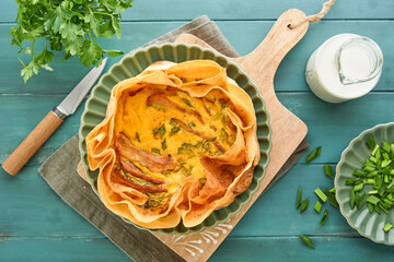 Homemade quiche or tart with slices of bacon and leeks with tortilla instead of dough on wooden...