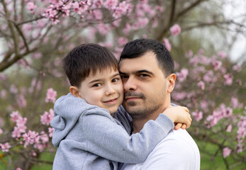 dad and son hugging against blossom pink tree in park. loving father with baby boy kid.happy fathers day holiday.spring time,easter is coming