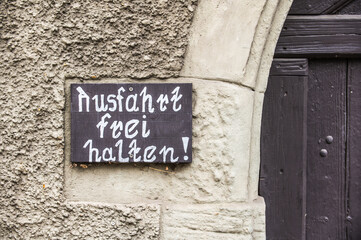 Hölzernes Hinweisschild Ausfahrt freihalten in alter Schrift  an steinernem Torbogen mit Holztor
