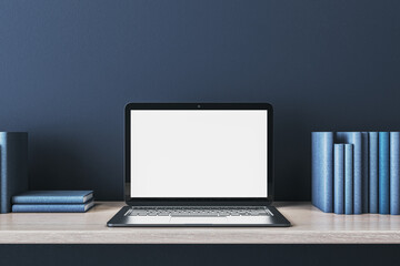 Fototapeta premium Close up of creative wooden designer desk with books and empty white mock up laptop screen on blue concrete wall. 3D Rendering.