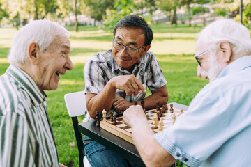 Group of senior friends playing chess at the park - obrazy, fototapety, plakaty