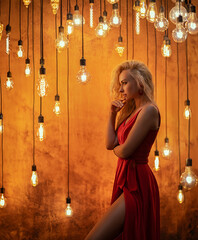 A beautiful blonde woman in a long red dress is looking at the LED Edison lamps in a retro style...