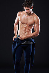 Studio, fitness and man in sports with swimwear, muscle and body from training, exercise for wellness. Dark background, champion and male person, performance and pride as athlete, health and workout